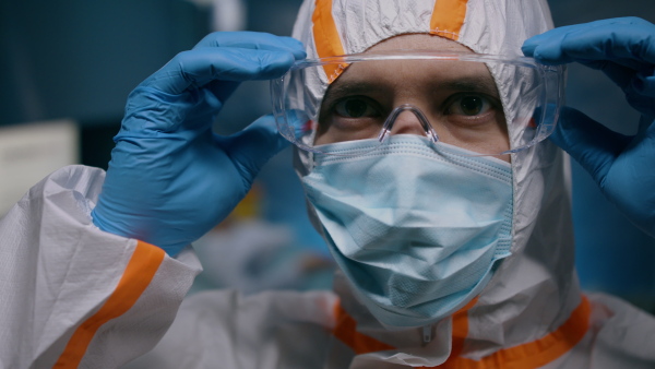 Doctor with protective suit and mask putting on glasses in hospital, coronavirus concept.