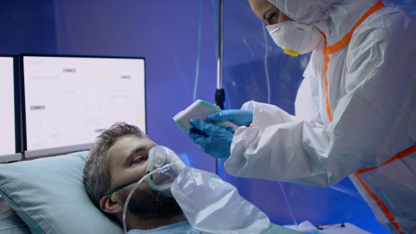 Doctor measuring temperature of infected patient in hospital, coronavirus concept.