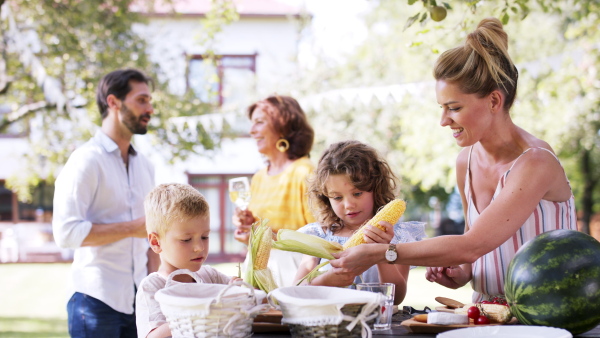 Large family having a garden party, kids peeling corn.