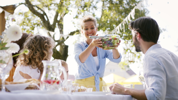 Large family having a big garden party and feasting together, woman bringing fresh salad.