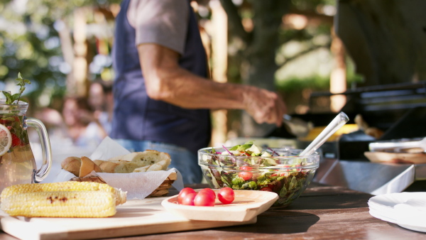 Large family having a garden party, focus on senior man barbecuing.