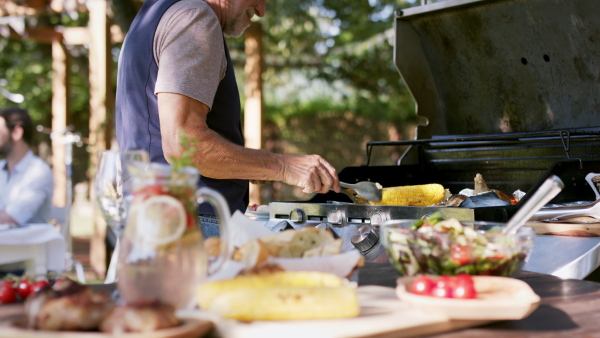 Large family having a garden party, senior man barbecuing.