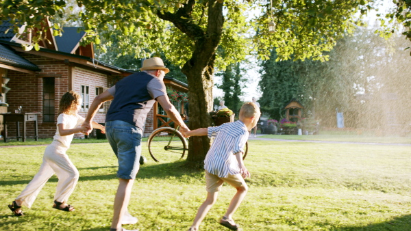 Large family having a garden party, grandfather running through stream of water with kids.