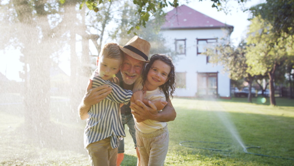 Large family having a garden party, grandfather grandfather standing under stream of water with kids, looking at camera.