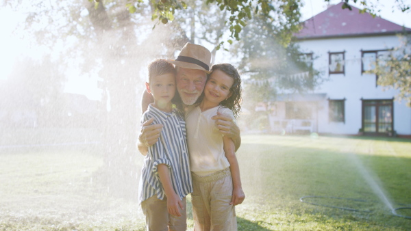 Large family having a garden party, grandfather grandfather standing under stream of water with kids, looking at camera.