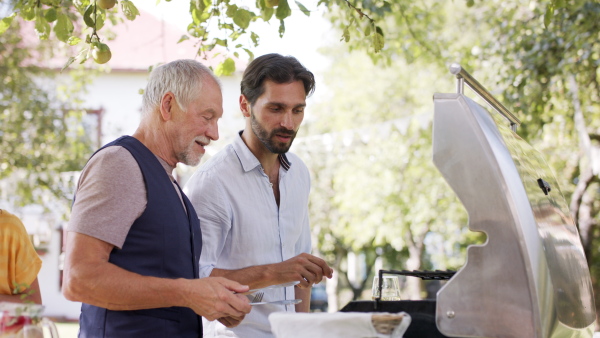 Large family having a garden party, father with son barbecuing.