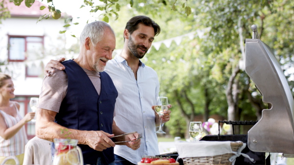 Large family having a garden party, father with son barbecuing.