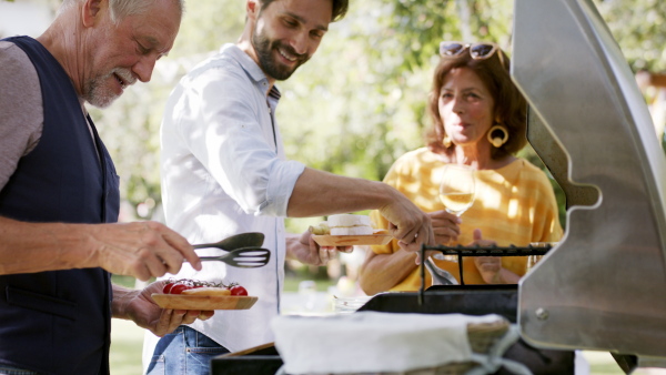 Large family having a garden party, father with son barbecuing.