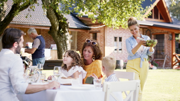 Large family having a big garden party and feasting together, woman bringing fresh salad.