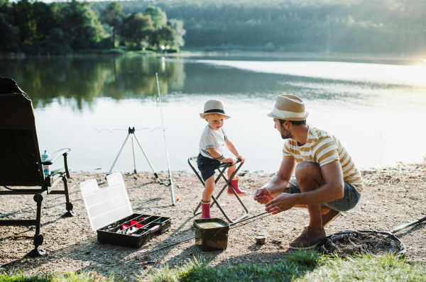 A mature father with a small toddler son outdoors fishing by a river or a lake.