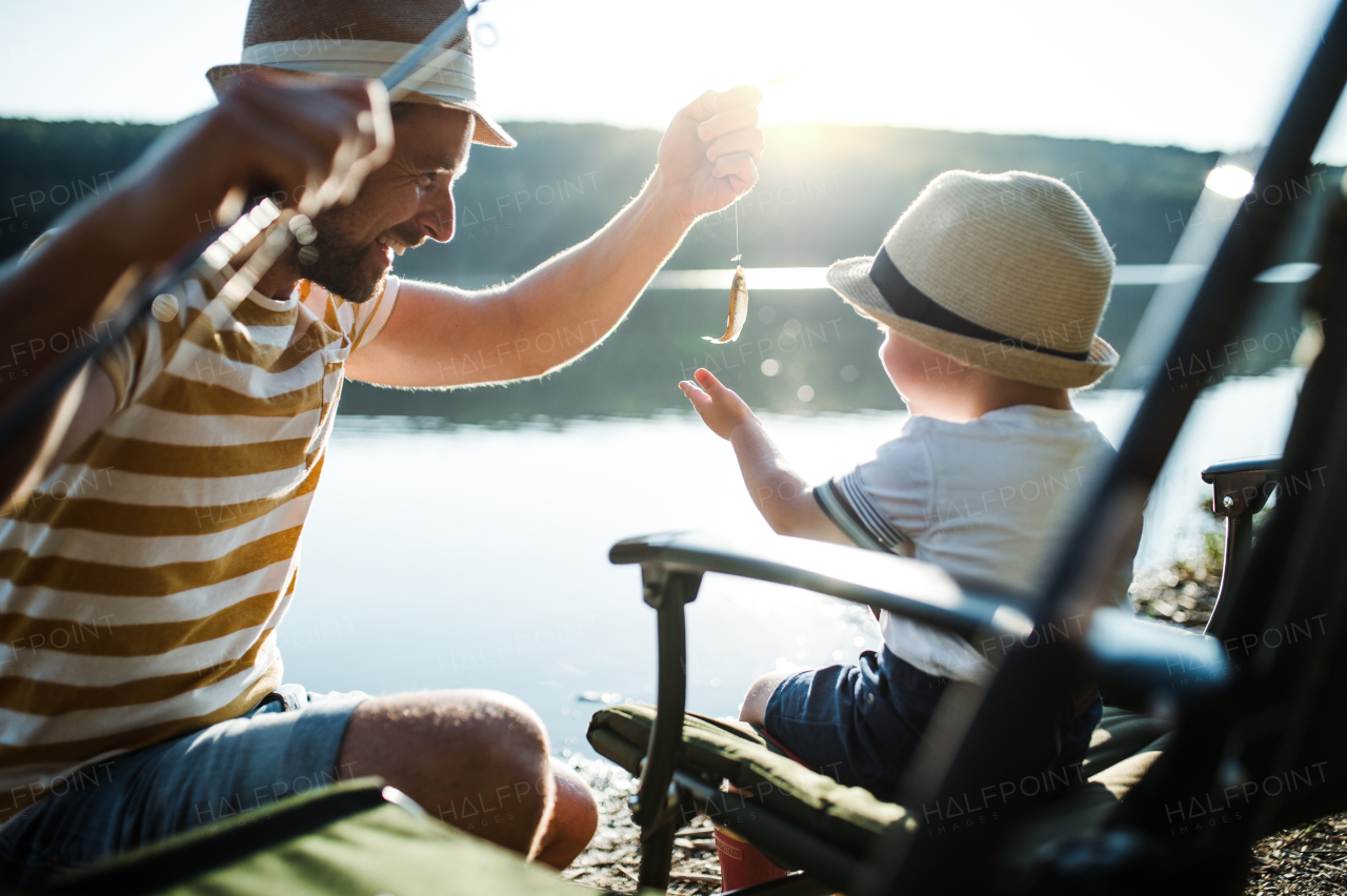 A mature father with a small toddler son outdoors fishing by a river or a lake.