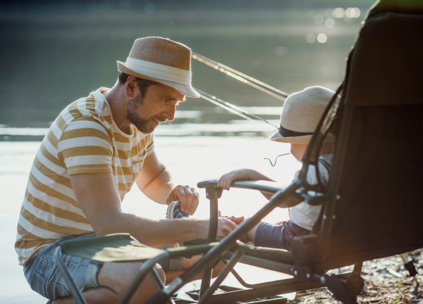 A mature father with a small toddler son outdoors fishing by a river or a lake, talking.