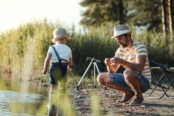 A mature father with a small toddler son outdoors fishing by a river or a lake.