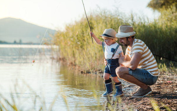 A mature father with a small toddler son outdoors fishing by a river or a lake.