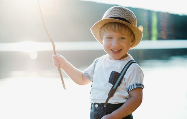 A small toddler boy with a hat standing by a lake at sunset. Copy space.