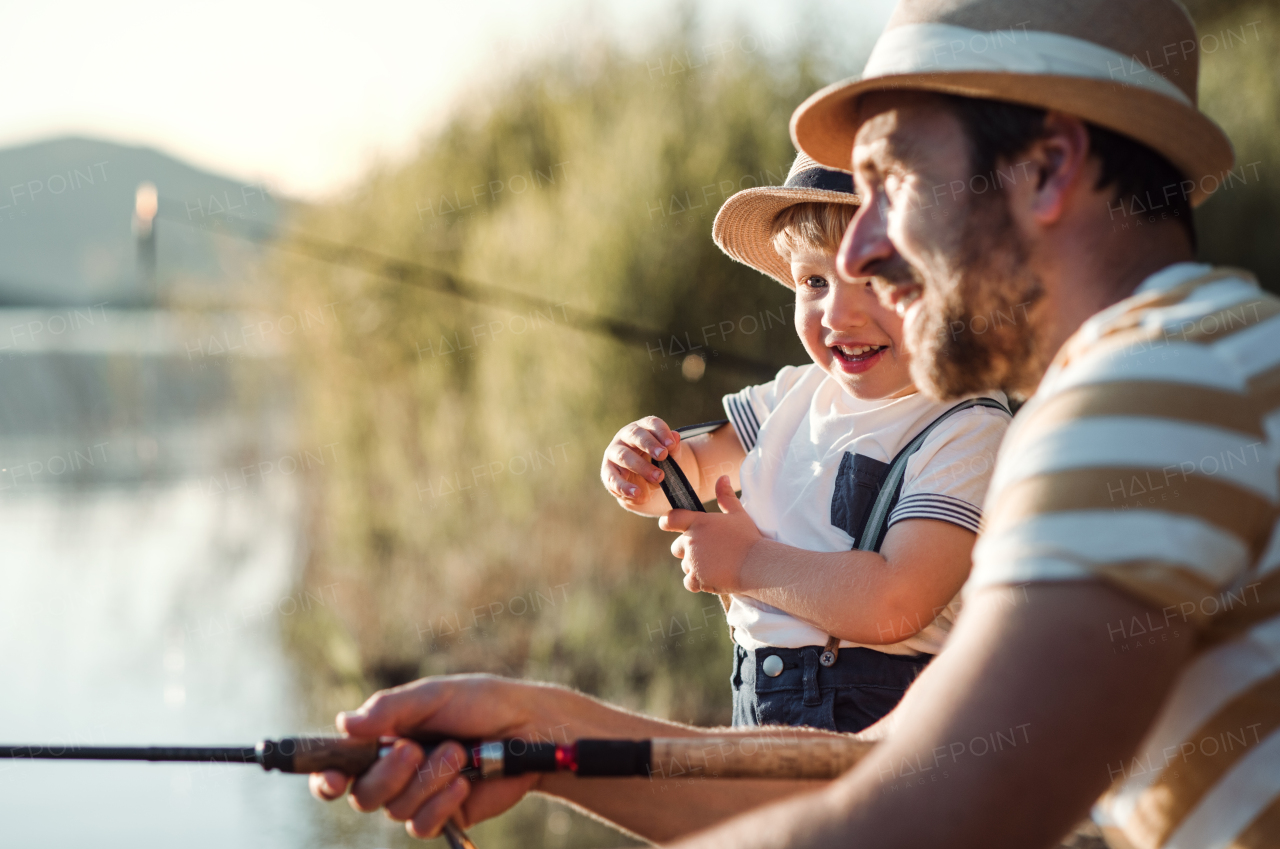 A mature father with a small toddler son outdoors fishing by a river or a lake.