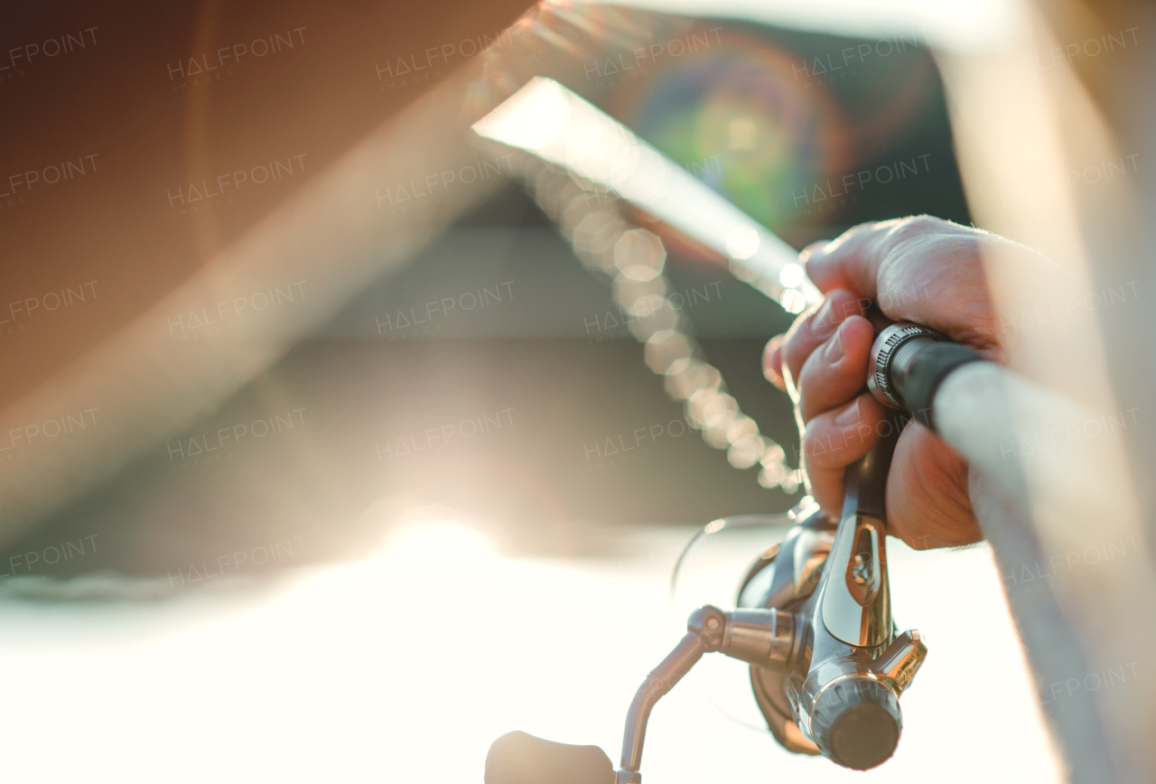 A midsection of a man fishing by a lake, holding a rod. A close-up.