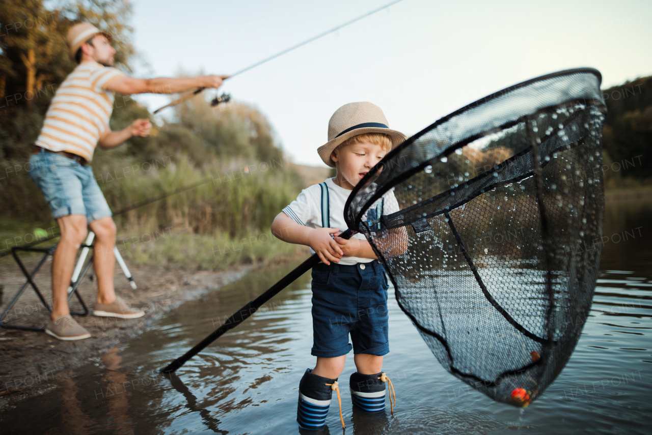 A mature father with a small toddler son outdoors fishing by a river or a lake.