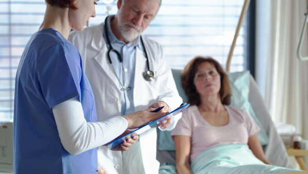 Portrait of senior male doctor standing in hospital room, talking to a female nurse.