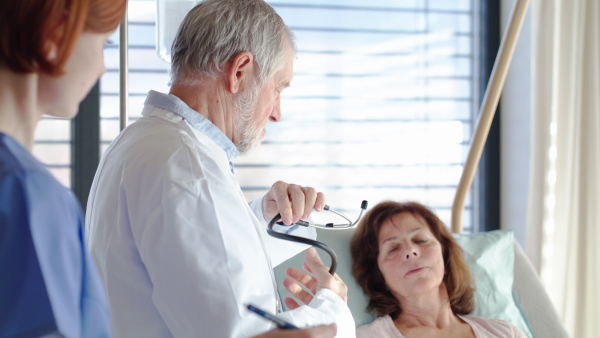 A senior doctor and nurse examining a woman patient with stethoscope in hospital.