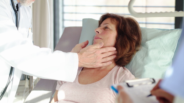 A senior male doctor examining a woman patient in hospital.