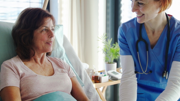 Friendly woman doctor or nurse talking to patient in bed in hospital, holding hands.