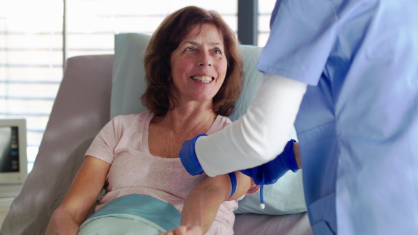 Unrecognizable doctor or nurse treating patient in bed in hospital, blood taking.