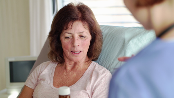 Unrecognizable female doctor talking to patient in bed in hospital about taking medication.