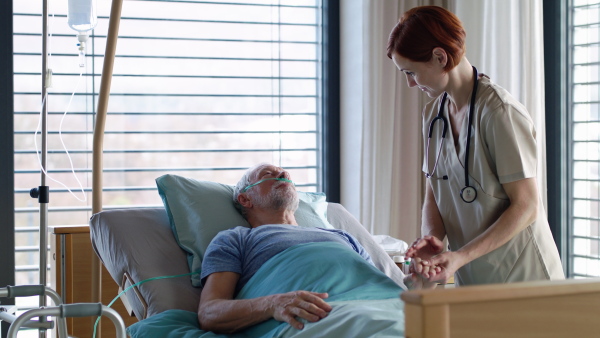 Friendly female doctor talking to senior patient in bed in hospital.