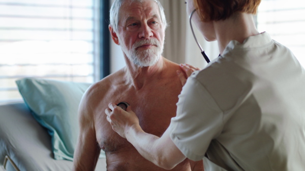 A friendly female doctor examinig a senior patient with stethoscope in bed in hospital.