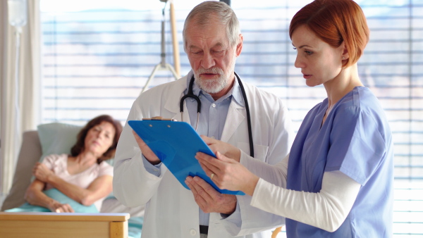 Portrait of senior male doctor standing in hospital room, talking to a female nurse.