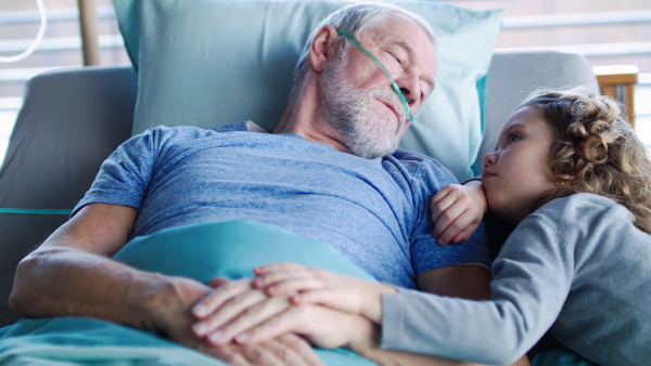 A small girl visiting ill grandfather in bed in hospital room, talking.