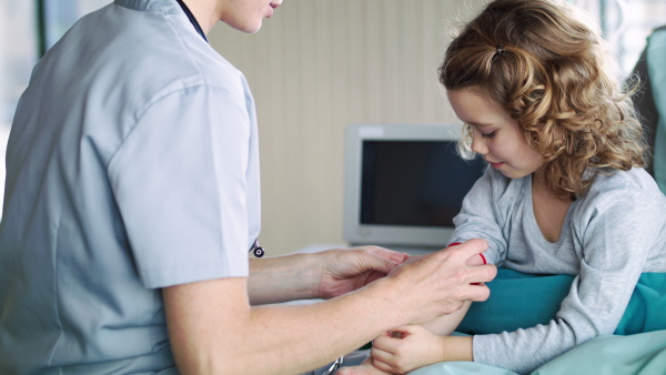 An unrecognizable female doctor examining small girl in bed in hospital.