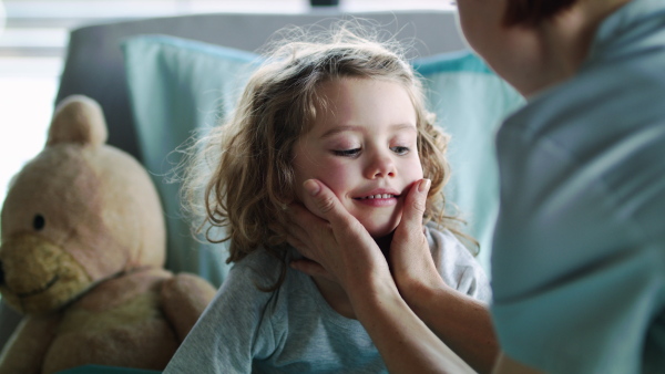 An unrecognizable female doctor examining small girl in bed in hospital.