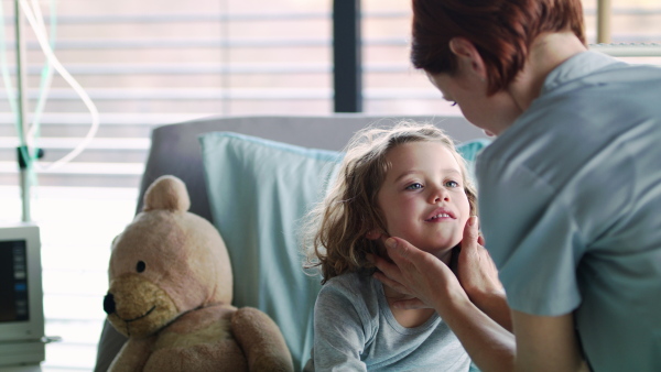 Woman doctor examining small girl in bed in hospital, feeling glands.