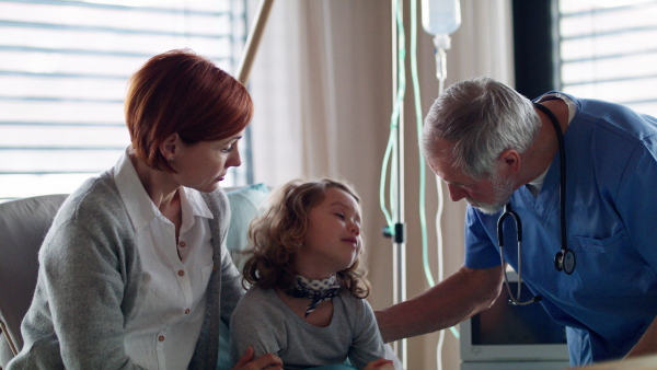 Senior doctor examining a small hospitalized girl with mother in hospital.