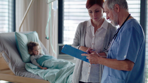 Senior doctor and mother of small hospitalized girl in hospital, talking.