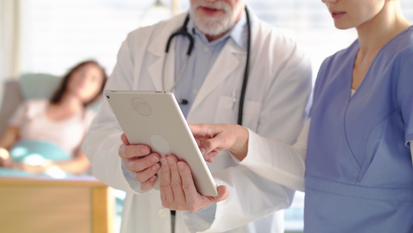 Unrecognizable man doctor with tablet standing in hospital room, talking to a nurse.