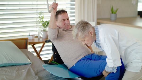 Healthcare worker helping paralysed senior patient into wheelchair in hospital or at home.