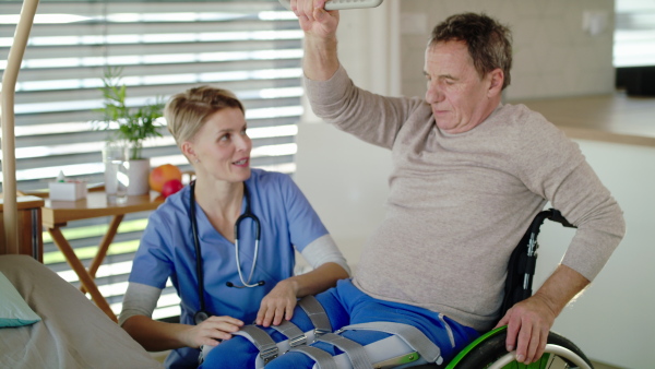 Healthcare worker and paralysed senior man patient in wheelchair in hospital, applying orthosis.