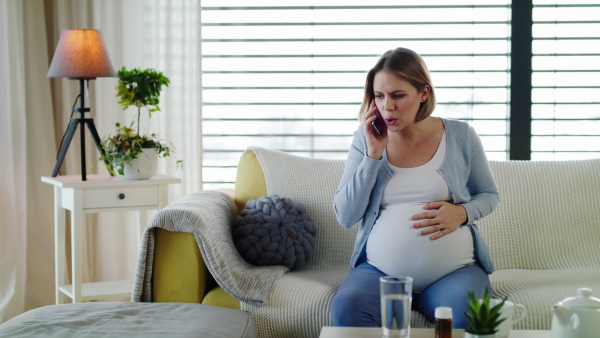 Portrait of pregnant woman in pain indoors at home, making emergency phone call.