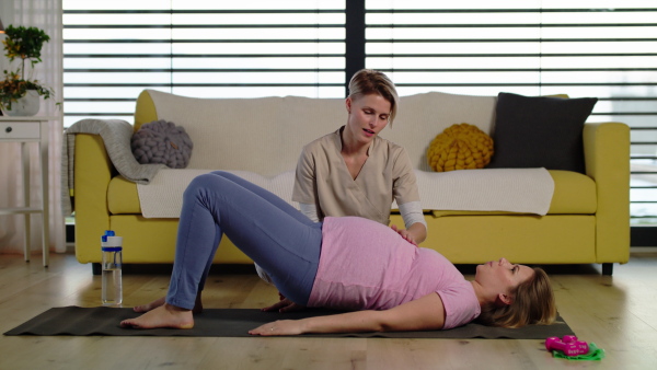 Pregnant woman doing exercise with instructor on the floor at home.