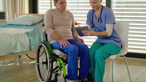 Healthcare worker with tablet and senior patient in wheelchair in hospital or at home, talking.