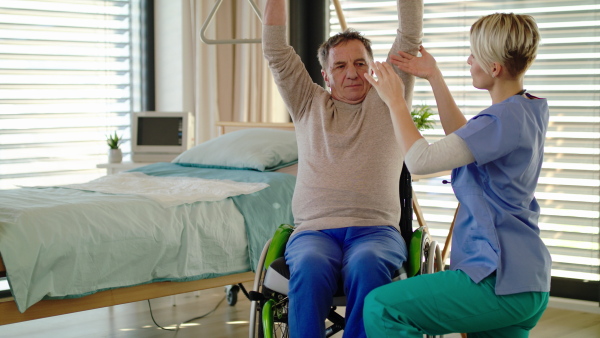 Healthcare worker and senior patient in wheelchair in hospital, physiotherapy with dumbbells.