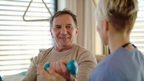 Healthcare worker and senior patient in wheelchair in hospital, physiotherapy with dumbbells.