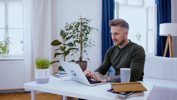 Side view of man with laptop working indoors at desk in home office, video call concept.