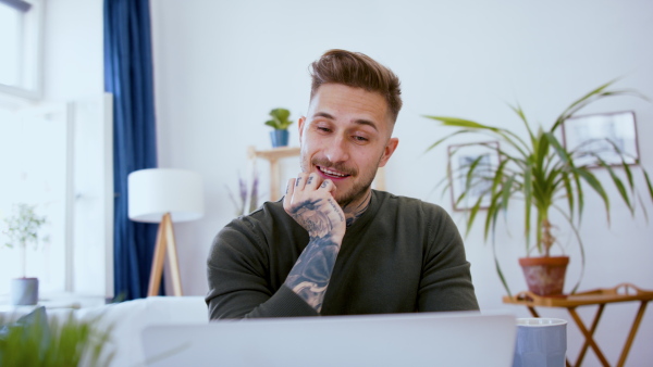 Front view of man with laptop working indoors at desk in home office, video call concept.