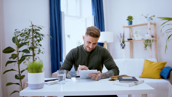 Young graphic designer with tablet sitting indoors at desk in home office, working.