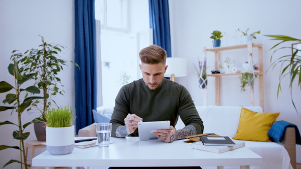 Young graphic designer with tablet sitting indoors at desk in home office, working.