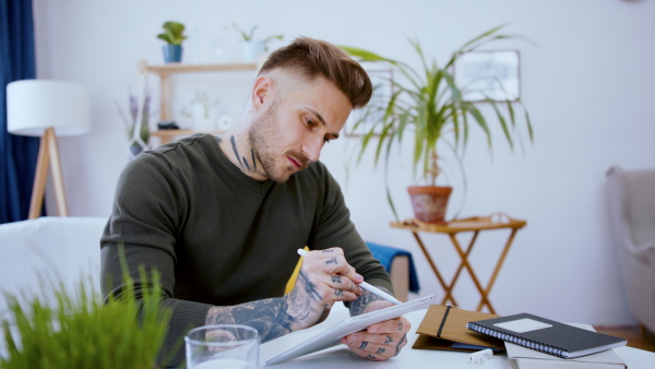 Young graphic designer with tablet sitting indoors at desk in home office, working.